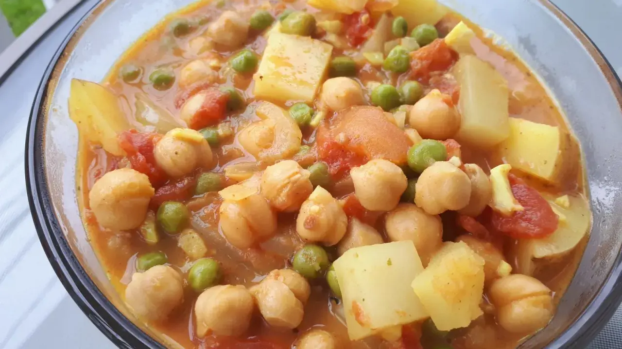 Un savoureux curry de petit pois avec des pois chiches et des morceaux de pommes de terre dans une sauce orangée.