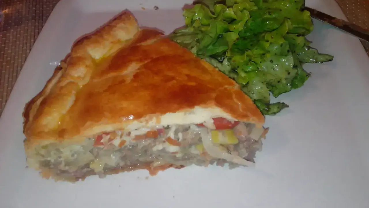 Une part de tourte à la viande grand-mère, dorée et généreuse, servie avec une salade verte croquante. Un délice réconfortant.