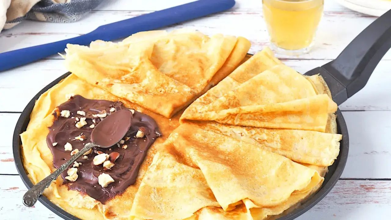Délicieux crepe a la biere, pliés dans une poêle, garnis de pâte à tartiner au chocolat et noisettes. Une cuillère repose sur le dessus.