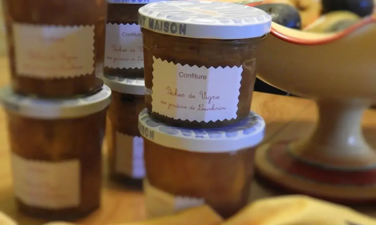 Plusieurs pots de confiture maison, dont une délicieuse confiture de pêches de vignes, sont alignés sur une table en bois.