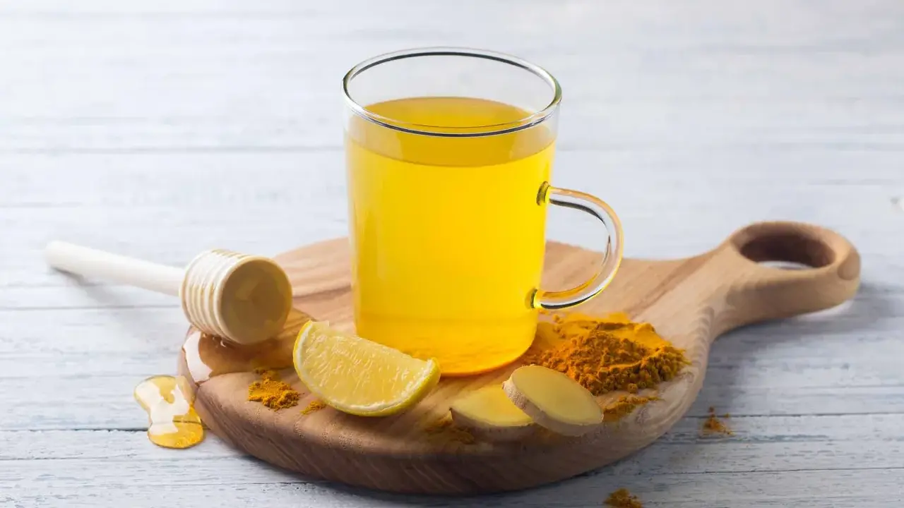 Une tasse de boisson gingembre citron curcuma, avec des tranches de citron, du gingembre frais et du curcuma en poudre.