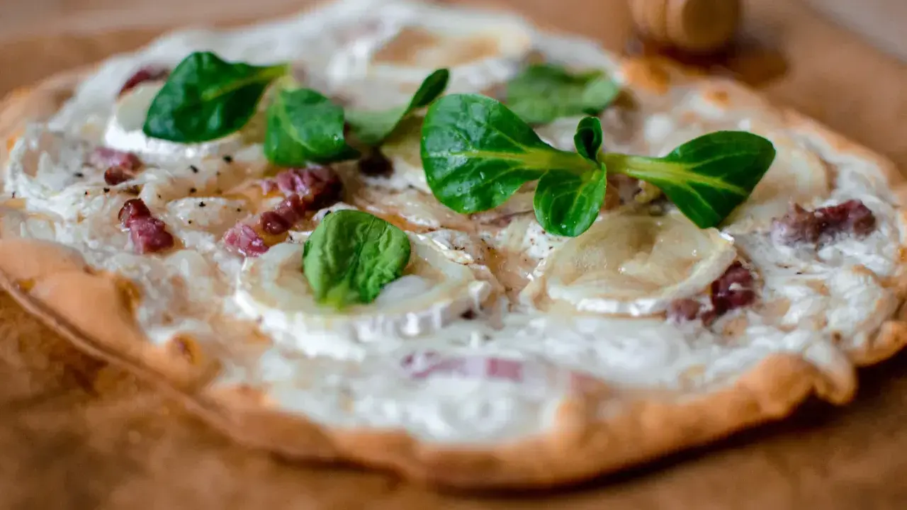 Délicieuse tarte flambée végétarienne garnie de fromage de chèvre, oignons et herbes fraîches.