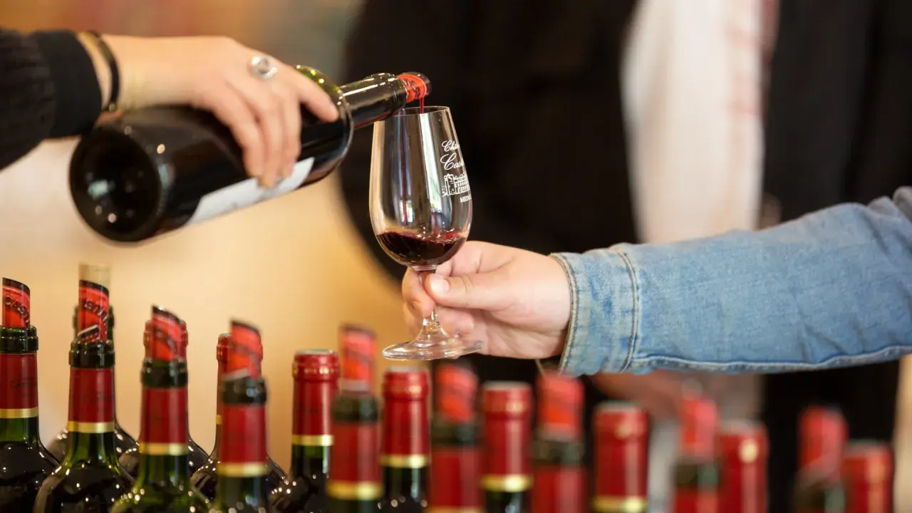 Service d'un vin rouge fruité et doux dans un verre, avec des bouteilles alignées en arrière-plan.