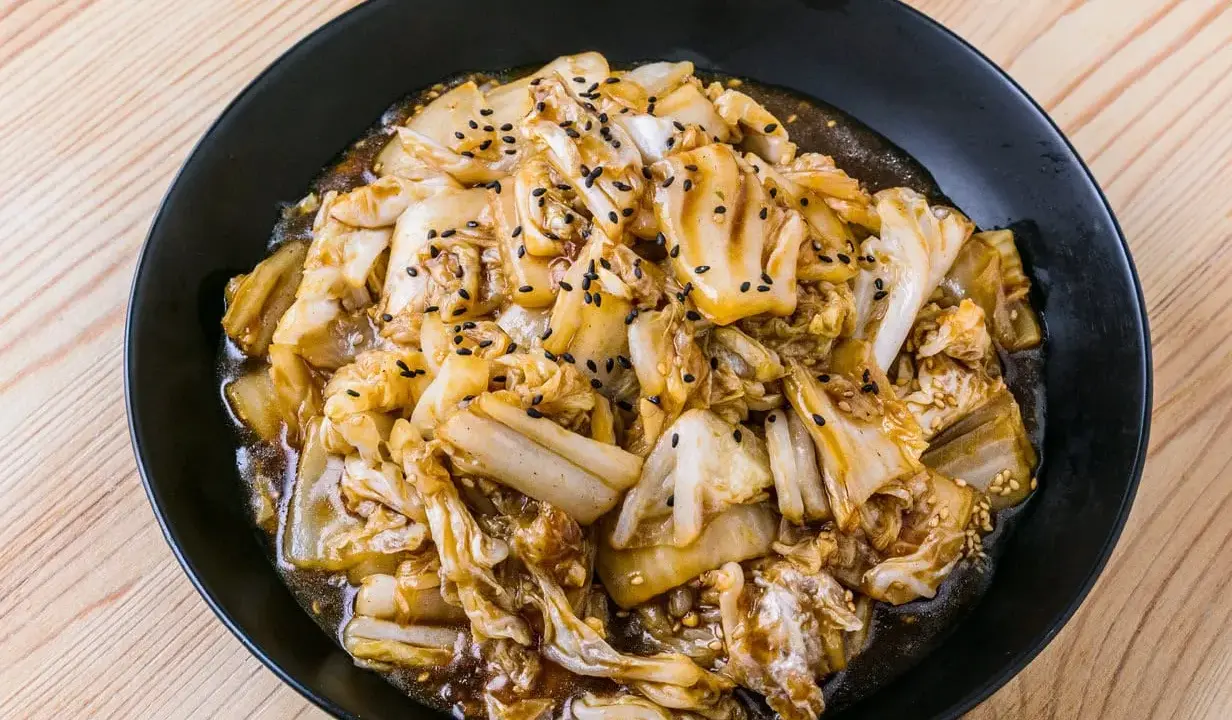 Un plat de recette pak choï sauté, garni de graines de sésame noires et blanches, sur une assiette noire.