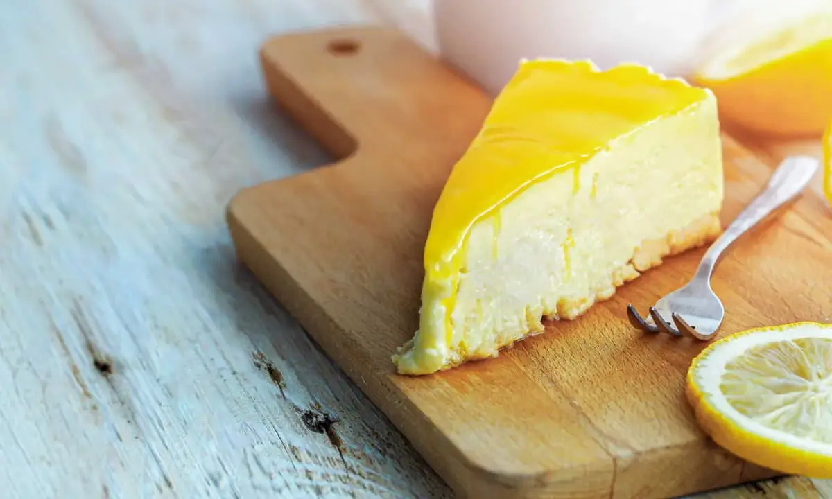 Tranche de cheesecake au citron, une recette Philadelphia sans cuisson, sur une planche en bois avec une fourchette et des rondelles de citron.