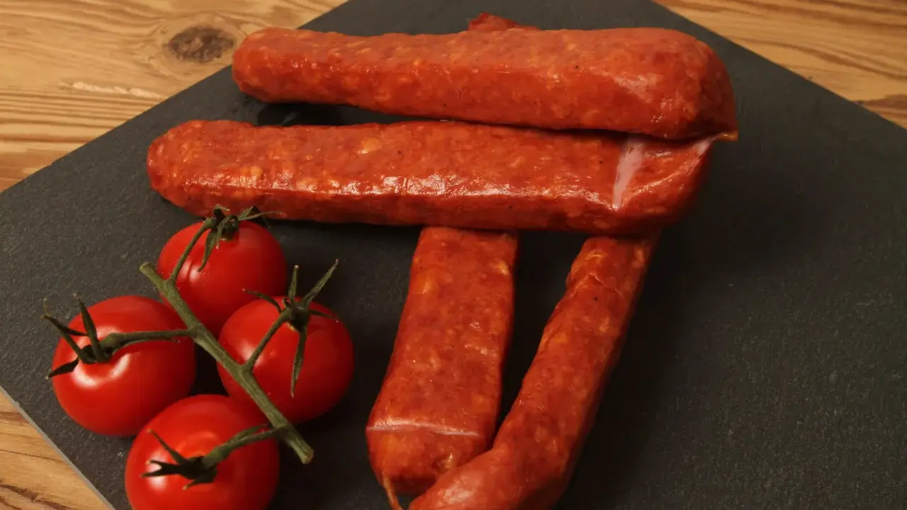 Saucisses sèches et tomates cerises sur une planche d'ardoise, parfait pour une recette de saucisse gendarme.