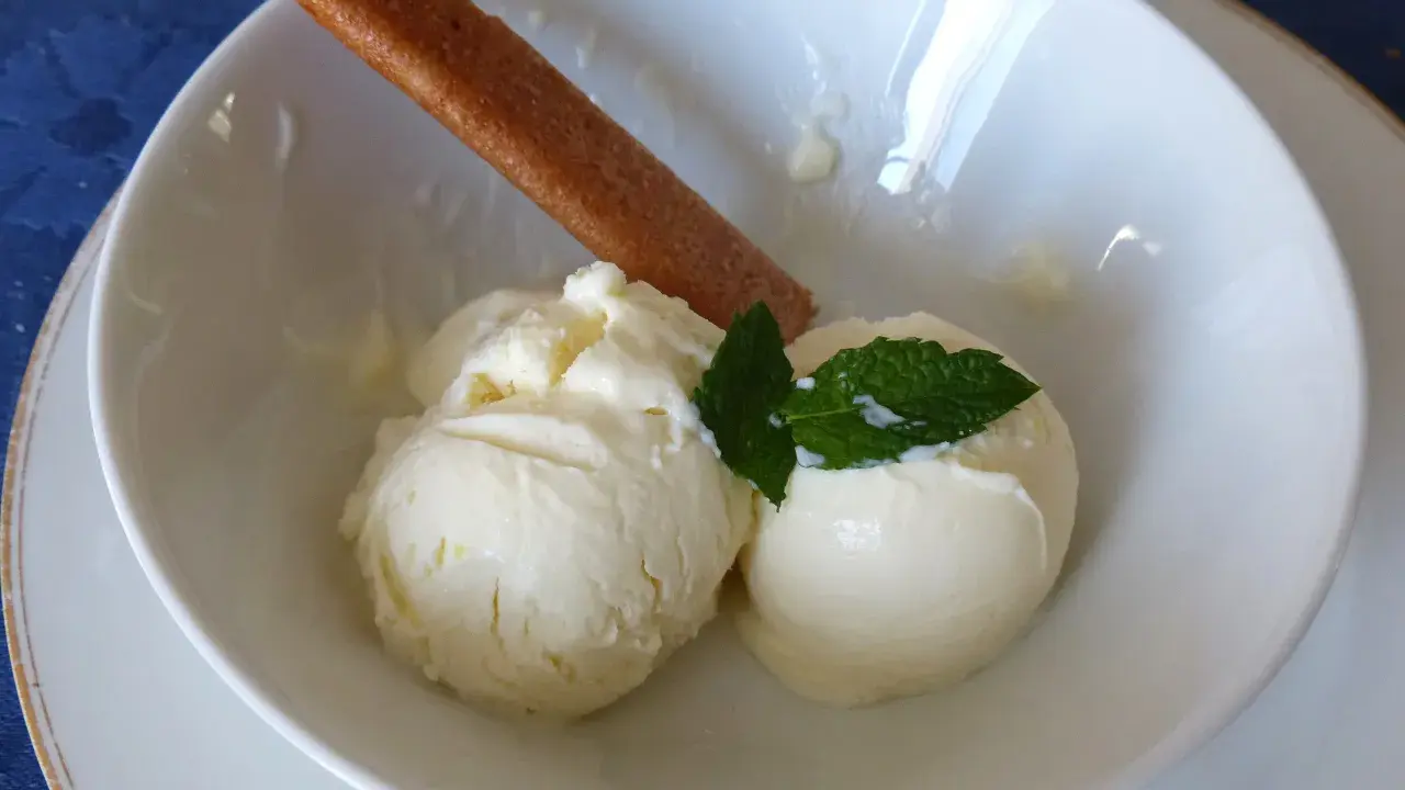 Deux boules de glace au citron onctueuse, garnies de menthe fraîche et d'un biscuit fin, dans un bol blanc.