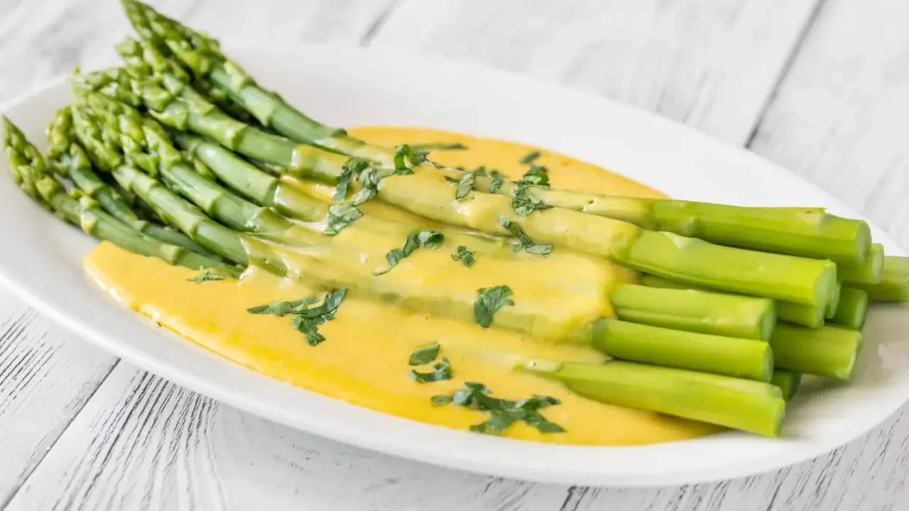 Un bouquet d'asperges vertes nappées d'une sauce hollandaise crémeuse, garnies de persil frais. Une délicieuse idée d'asperges en entrée froide.