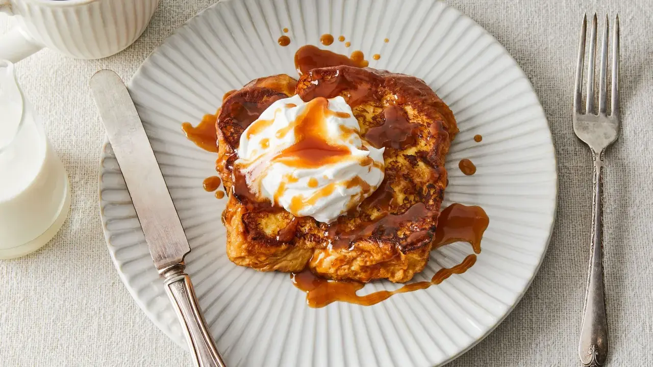 Pain perdu gourmand nappé d'une sauce caramel au miso, garni de crème fouettée. Servi avec une tasse de café et un verre de lait.