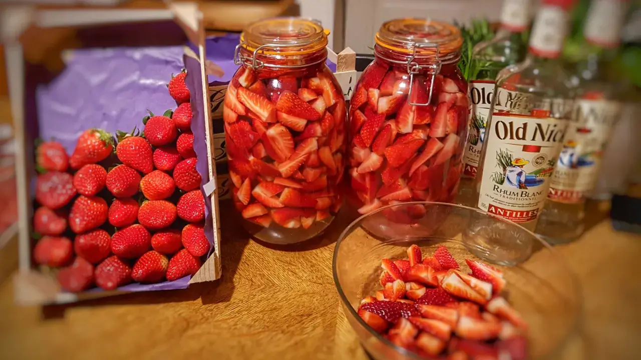 Bocaux de fraises coupées prêtes pour un rhum arrangé fraise menthe. Bouteilles de rhum à proximité.