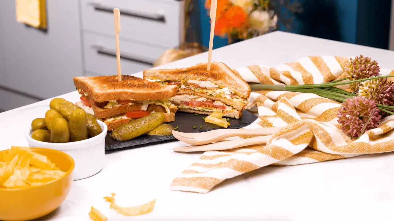 Un délicieux club sandwich, garni de tomates et de laitue, servi avec des cornichons et des chips.