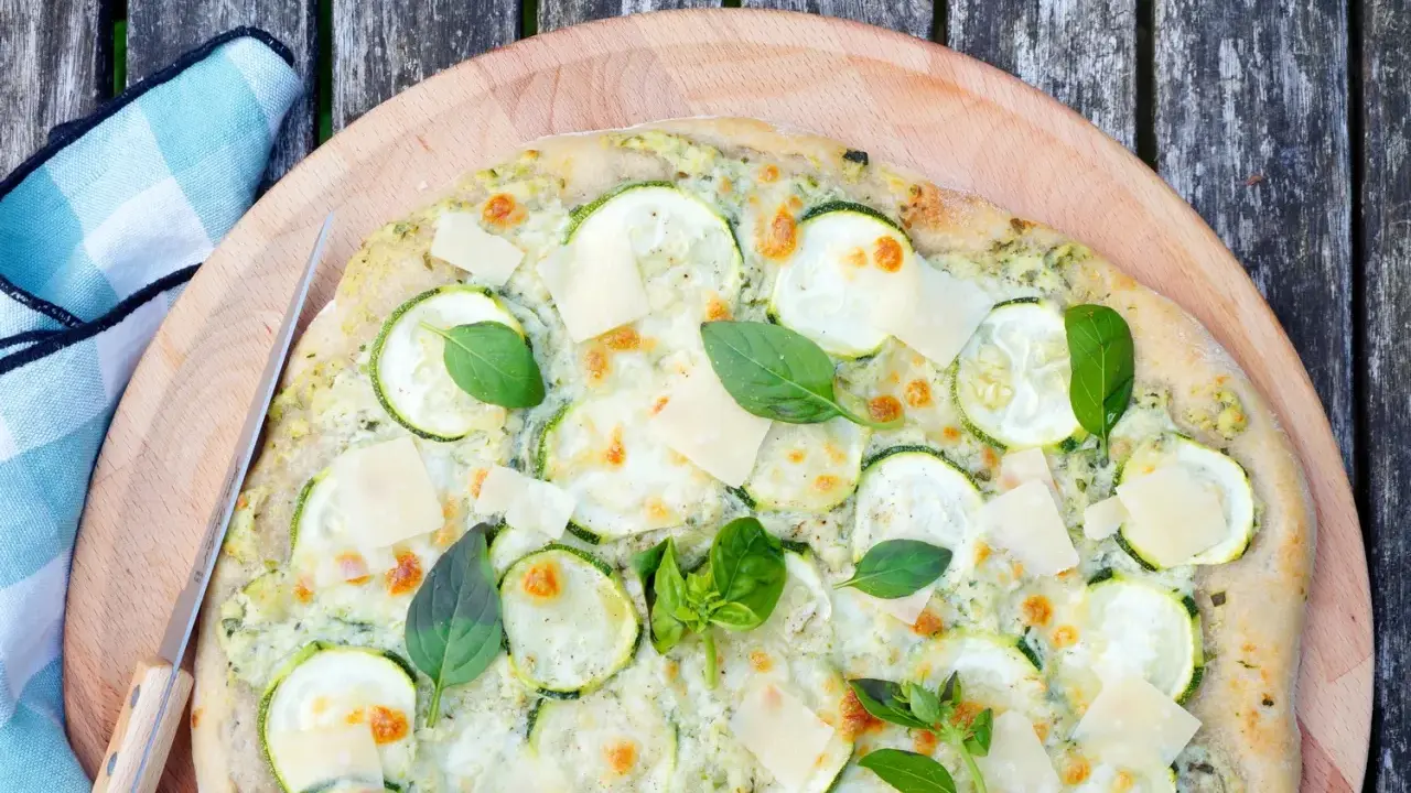 Délicieuse pizza courgette, garnie de fromage fondant, de fines tranches de courgette et de feuilles de basilic frais, prête à être dégustée.