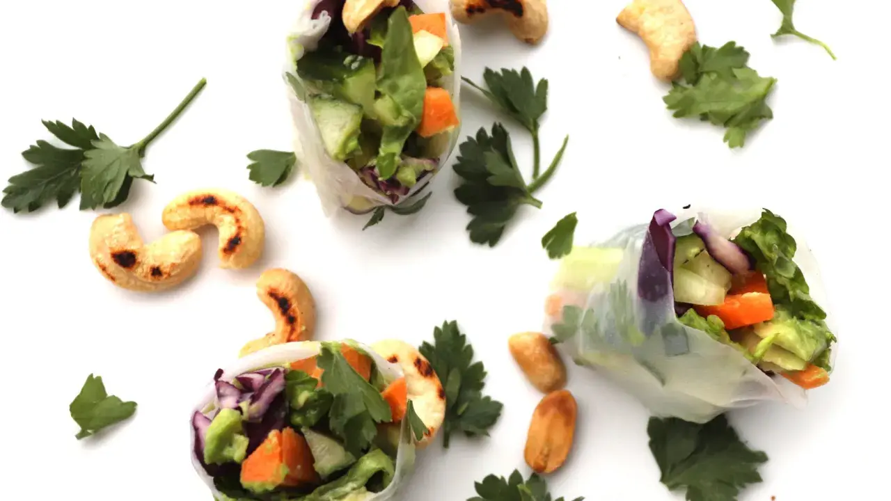 Trois rouleaux de printemps végétariens colorés, remplis de légumes frais et de noix de cajou grillées, parsemés de persil frais.