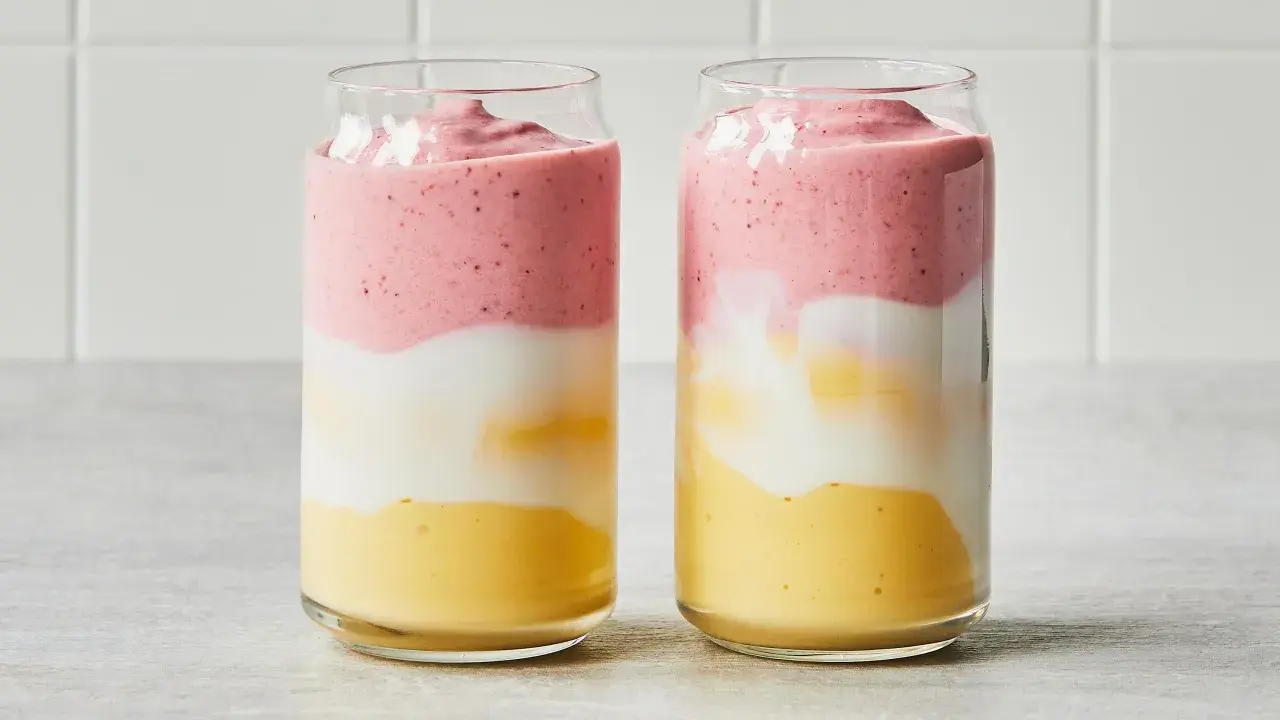 Deux verres de smoothie sans lait aux couches distinctes : jaune, blanc et rose.