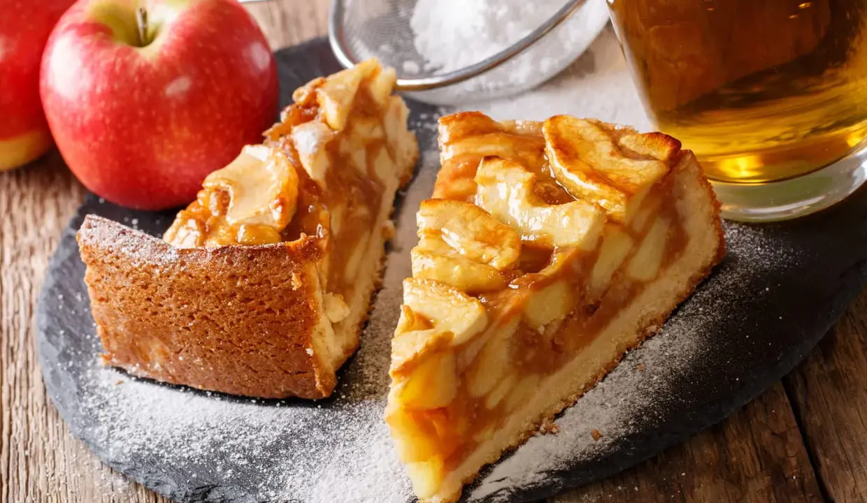 Deux parts de tarte aux pommes, saupoudrées de sucre glace, avec des pommes fraîches et un verre de cidre. Une belle idée de que faire avec des pommes.