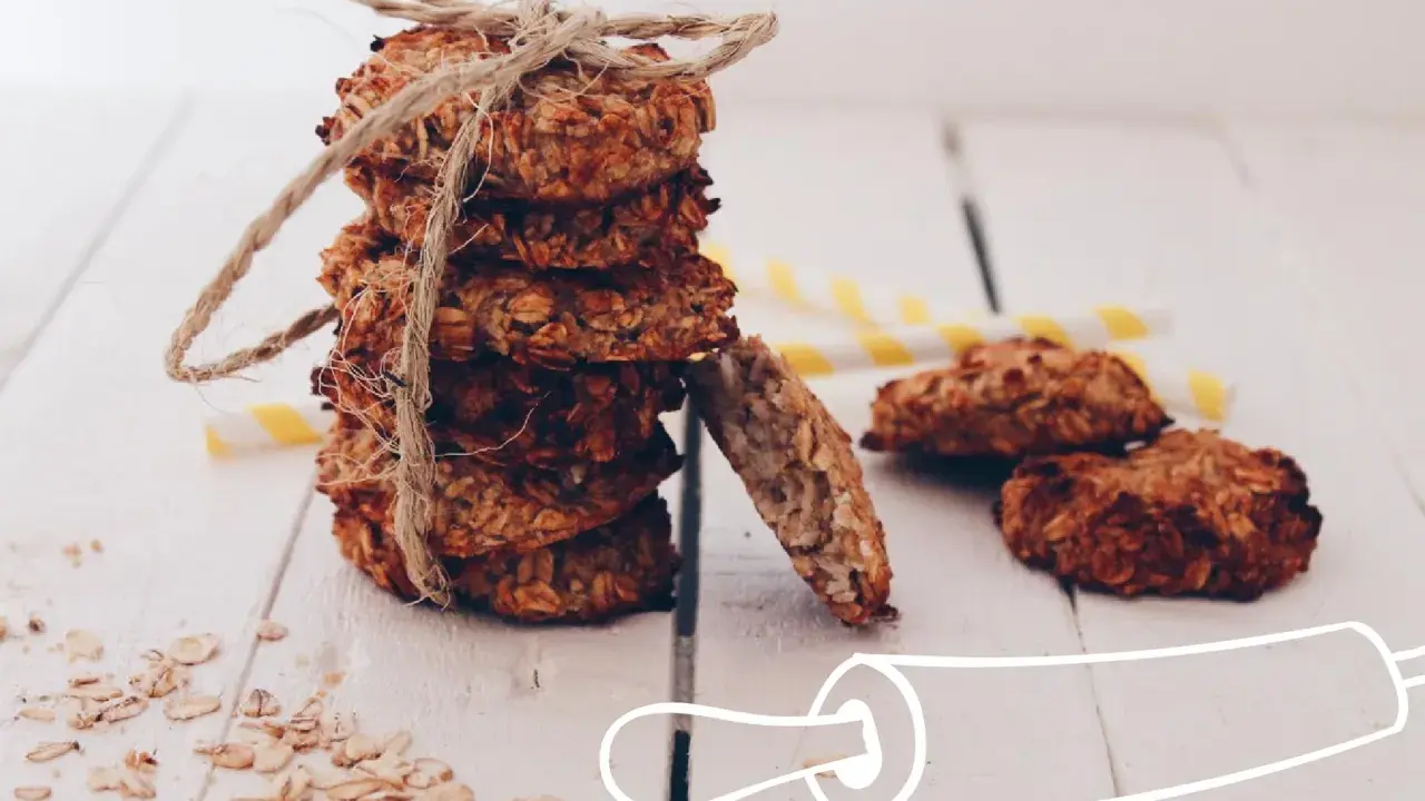 Pile de cookies healthy flocons d'avoine, liés par une cordelette. Quelques flocons éparpillés et des pailles rayées en arrière-plan.