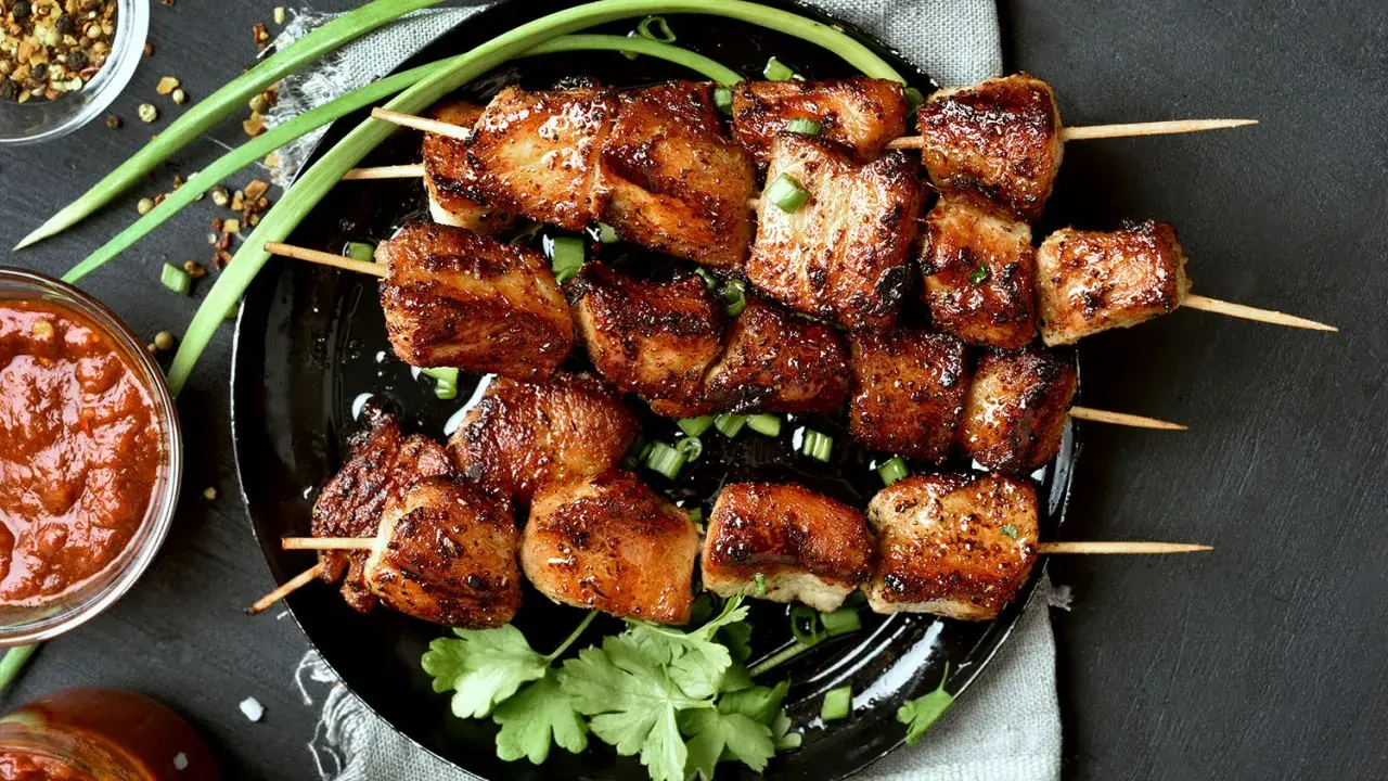 Brochettes de porc mariné, grillées à la perfection, garnies d'oignons verts et de coriandre fraîche. Accompagnées d'une sauce épicée.