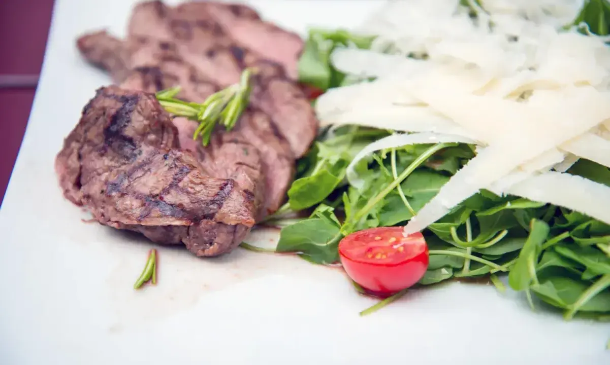 Délicieuse tagliata de boeuf grillée, servie avec une salade verte, copeaux de parmesan et une moitié de tomate cerise.