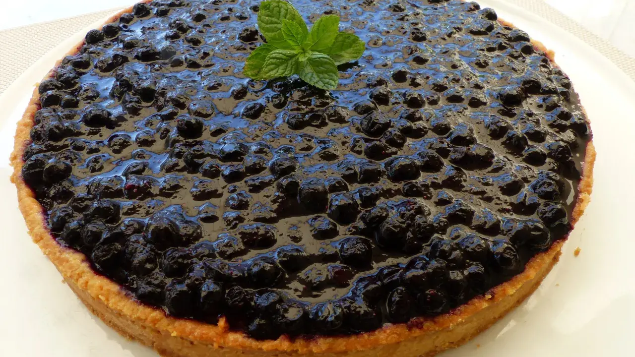 Tarte myrtille amande, une gourmandise aux myrtilles juteuses et à la pâte sablée aux amandes, décorée d'une touche de menthe fraîche.