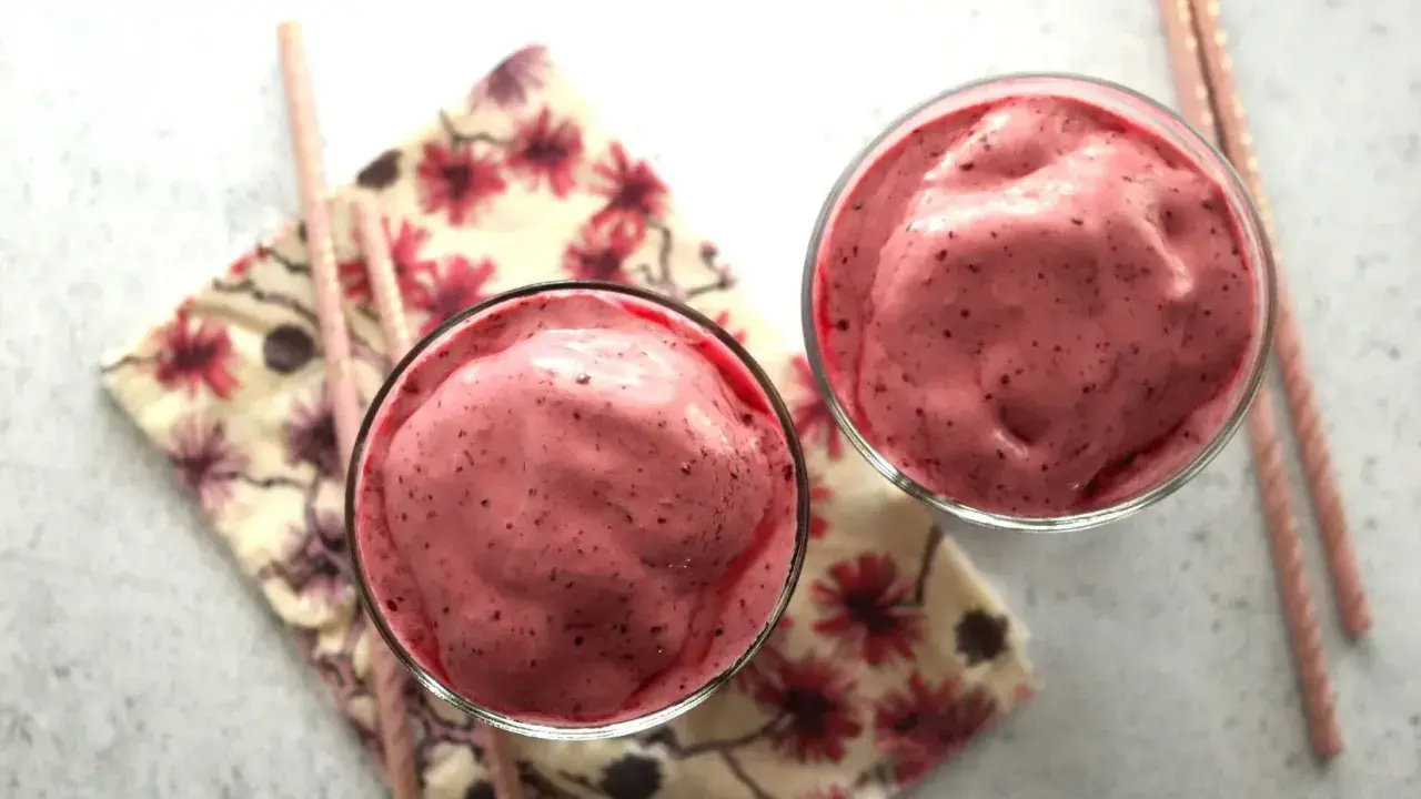 Deux verres remplis d'un onctueux milkshake fruit rouge, accompagnés de pailles roses et d'une serviette fleurie.