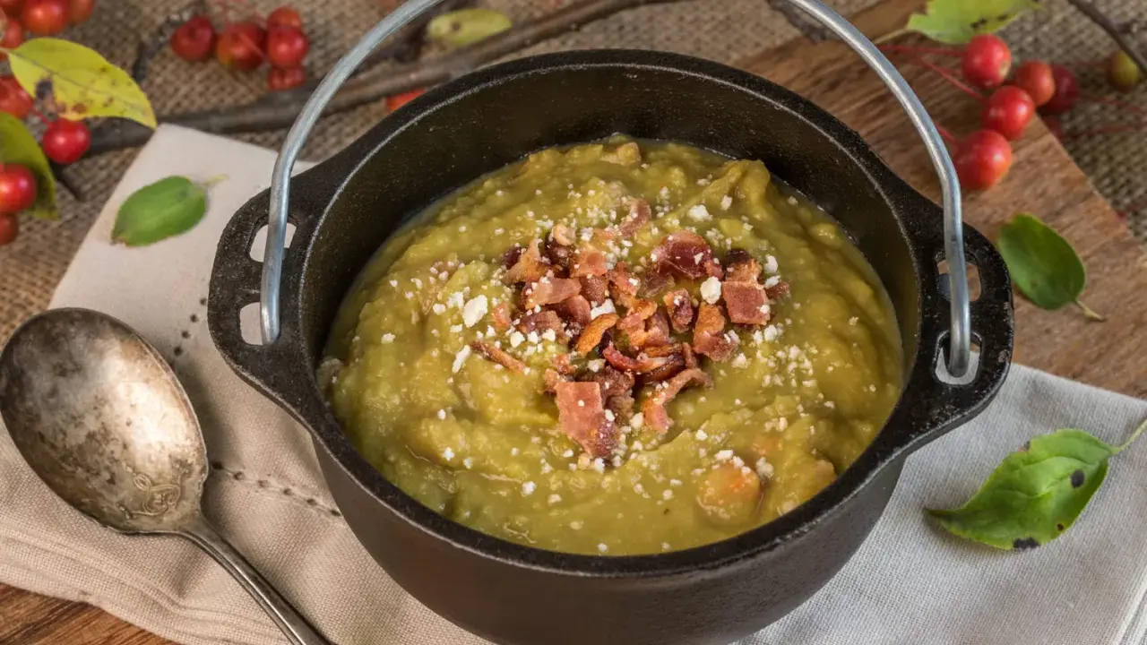 Soupe de pois cassés réconfortante, garnie de lardons croustillants et de fromage râpé, servie dans une cocotte en fonte rustique.