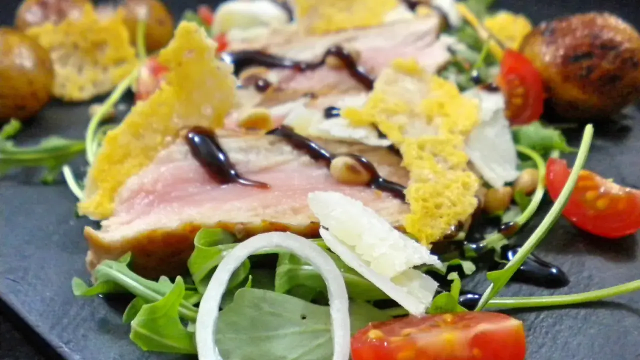 Délicieuse tagliata de veau, servie sur un lit de roquette avec des tomates cerises, des oignons et des tuiles de parmesan croustillantes.