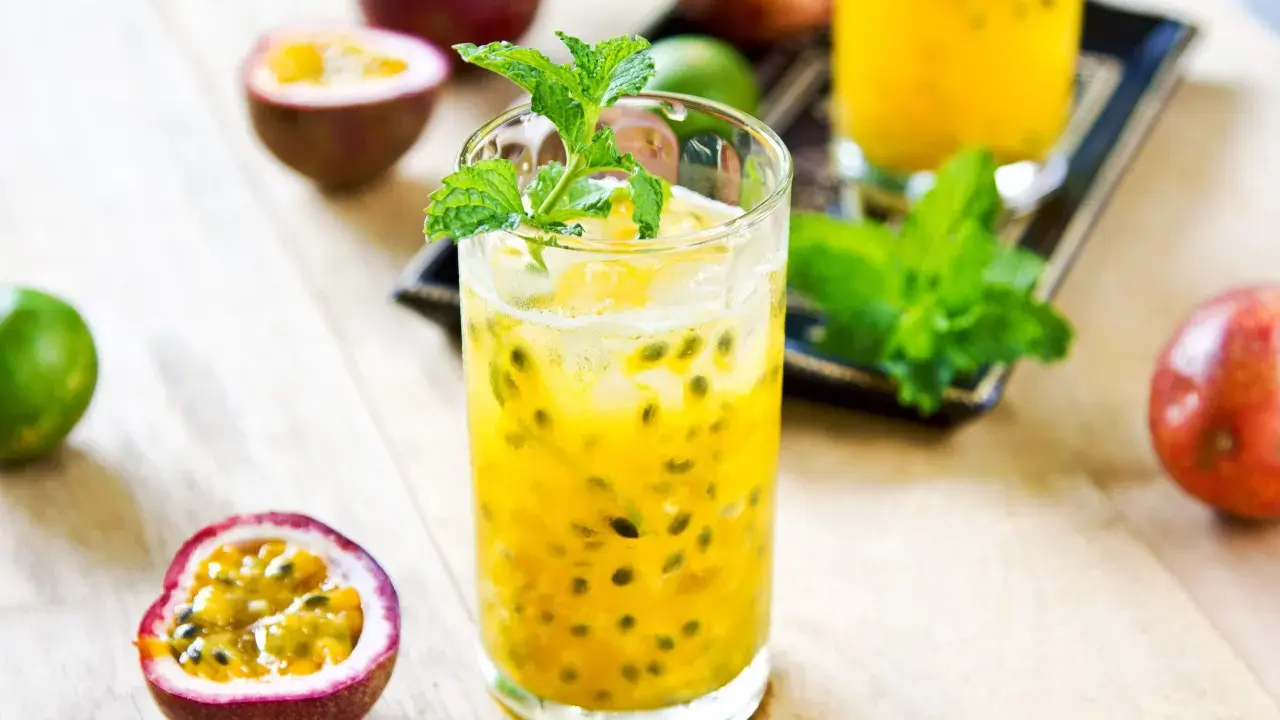 Un verre de cocktail fruit de la passion, garni de menthe fraîche, entouré de fruits entiers et coupés.