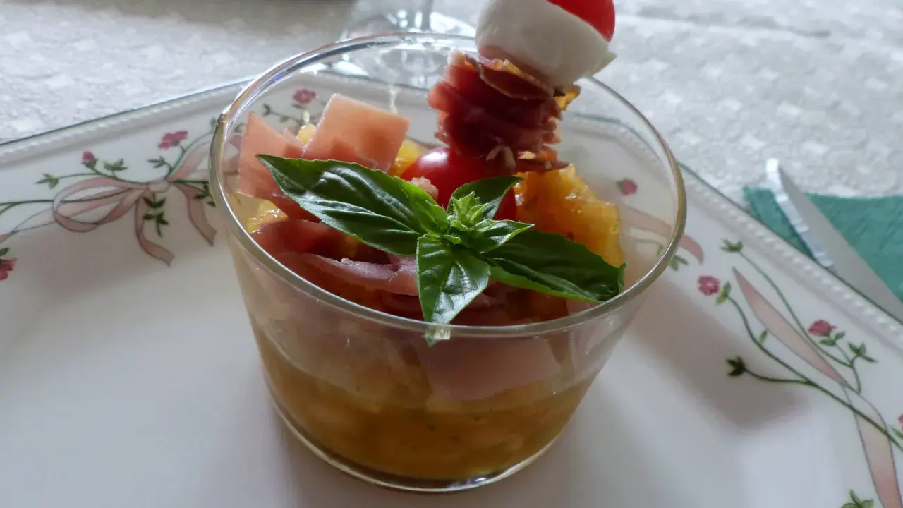 Verrine melon jambon cru : dés de melon, jambon cru, mozzarella et tomate cerise sur un pic. Une feuille de basilic décore ce délice.