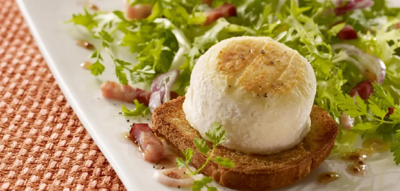 Une délicieuse salade de chèvre chaud sur toast, garnie de lardons et de persil frais, sur une assiette blanche.