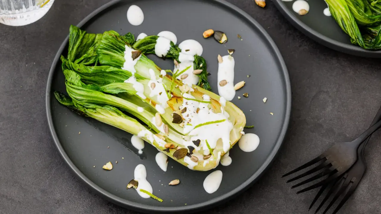 Une assiette de pak choi cru arrosé d'une sauce crémeuse, garni de graines et de zeste de citron vert.