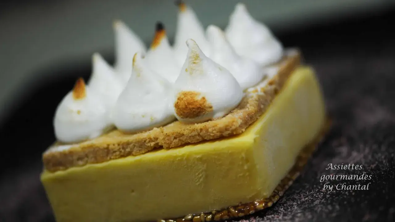 Une tranche de tarte au citron meringuée, avec sa crème jaune pâle, sa fine couche de biscuit et ses pointes de meringue légèrement caramélisées.