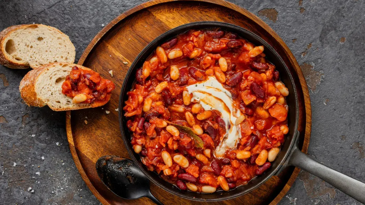 Délicieuse recette baked beans dans une poêle, garnie de crème, servie avec du pain grillé. Un plat réconfortant et savoureux.
