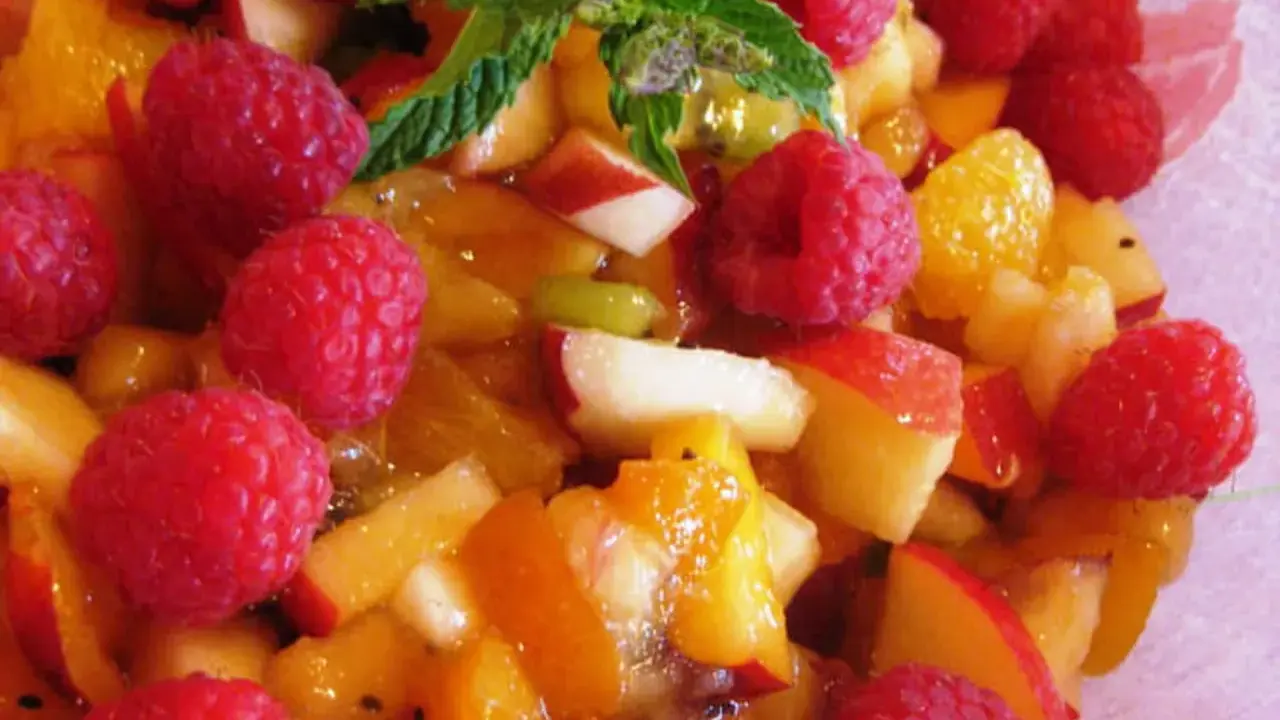 Une délicieuse salade de fruits d'été, pleine de framboises, pêches et abricots juteux, garnie de menthe fraîche.