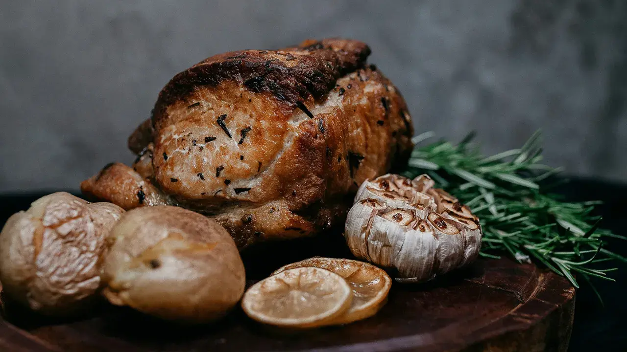 Un délicieux roti de veau au four, accompagné de pommes de terre rôties, d'ail confit, de rondelles de citron et de romarin frais sur une planche en bois.