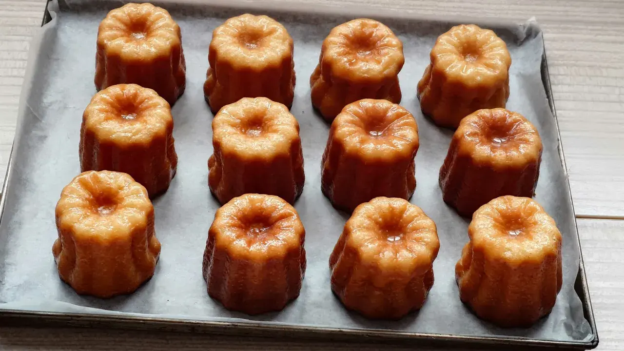 Douze mini cannelés dorés et caramélisés, prêts à être dégustés. Une recette facile pour des cannelés parfaits.