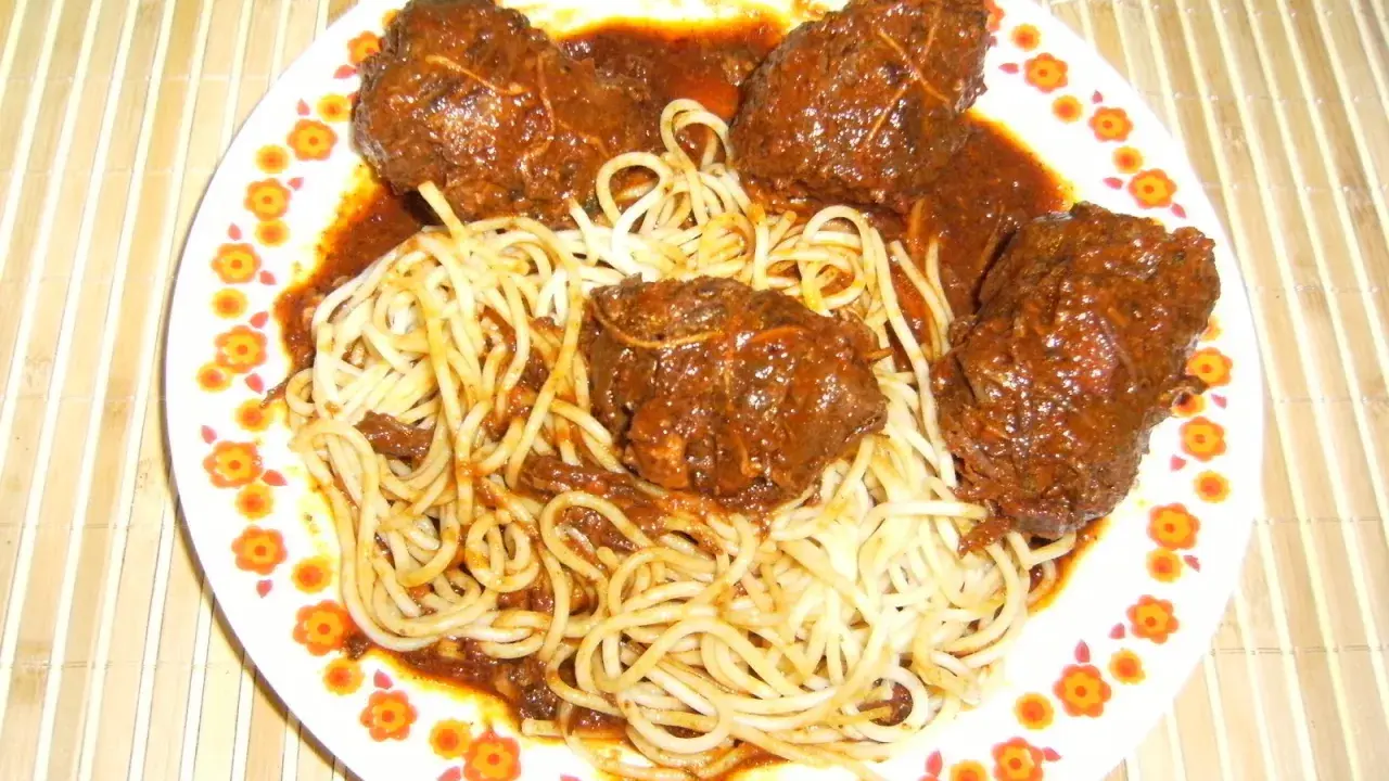 Un plat de spaghetti avec des ragoûts de bœuf en sauce, ressemblant à des alouettes sans tête, sur une assiette décorée de fleurs.