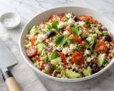Salade de riz colorée avec tomates, concombre, olives, feta et menthe fraîche. Un plat estival parfait.