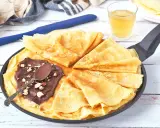 Délicieux crepe a la biere, pliés dans une poêle, garnis de pâte à tartiner au chocolat et noisettes. Une cuillère repose sur le dessus.