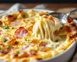 Un gratin d'endives à la béchamel réconfortant, avec du fromage fondant et des lardons croustillants. Une cuillère en prélève une portion généreuse.