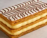 Un millefeuille croustillant avec une crème pâtissière onctueuse et un glaçage blanc décoré de volutes chocolatées.
