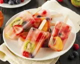 Plusieurs bâtonnets de glace à l'eau fruitée, remplis de fraises, kiwis, pêches et myrtilles, sur une assiette blanche.