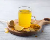Une tasse de boisson gingembre citron curcuma, avec des tranches de citron, du gingembre frais et du curcuma en poudre.
