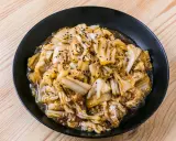 Un plat de recette pak choï sauté, garni de graines de sésame noires et blanches, sur une assiette noire.