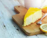 Tranche de cheesecake au citron, une recette Philadelphia sans cuisson, sur une planche en bois avec une fourchette et des rondelles de citron.