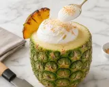 Un délice tropical : un pina colada sans alcool servi dans un ananas évidé, garni de crème et de noix de coco râpée.