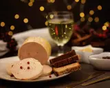 Tranche de foie gras sur une assiette, accompagnée de pain d'épices et d'un verre de vin blanc. Ambiance festive avec des lumières scintillantes.