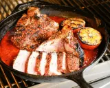 Un savoureux t bone de veau, coupé en tranches, mijote dans une sauce rouge avec des quartiers d'orange grillés dans une poêle en fonte sur un grill.