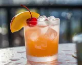 Cocktail rafraîchissant au jus d'abricot et alcool, garni d'une cerise et d'une tranche de pêche.