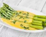 Un bouquet d'asperges vertes nappées d'une sauce hollandaise crémeuse, garnies de persil frais. Une délicieuse idée d'asperges en entrée froide.