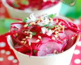 Salade de radis rose râpé et en tranches, garnie de graines de sésame et d'herbes fraîches, servie dans un petit pot.